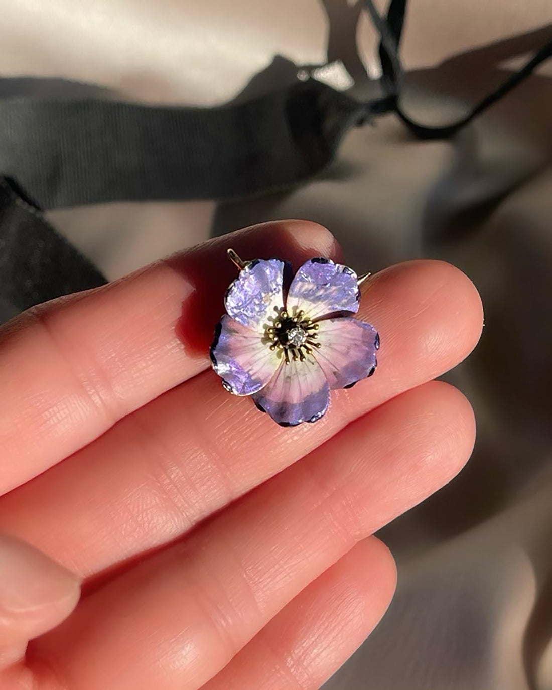 An antique edwardian art nouveau purple, pink, white, and black enamel dogwood flower brooch and pendant with an Old Mine Cut diamond, shown in hand