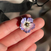 An antique edwardian art nouveau purple, pink, white, and black enamel dogwood flower brooch and pendant with an Old Mine Cut diamond, shown in hand