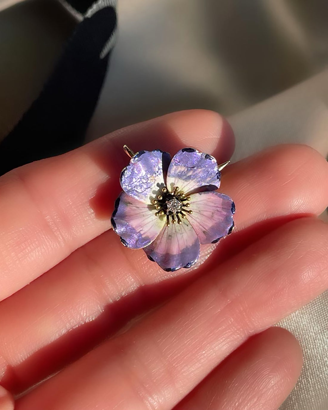 An antique edwardian art nouveau purple, pink, white, and black enamel dogwood flower brooch and pendant with an Old Mine Cut diamond, shown in hand