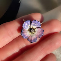 An antique edwardian art nouveau purple, pink, white, and black enamel dogwood flower brooch and pendant with an Old Mine Cut diamond, shown in hand