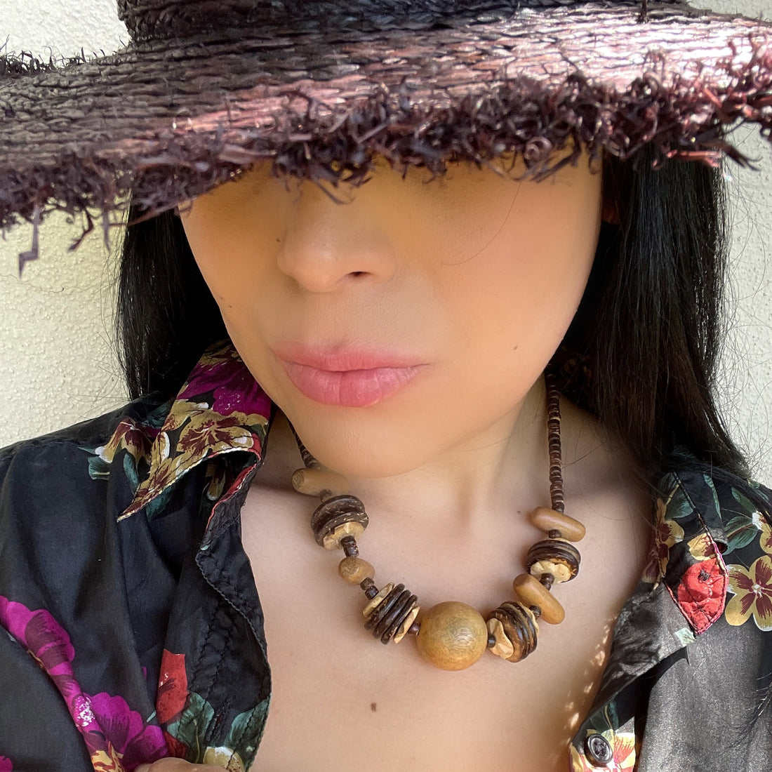 A vintage 1970s wooden bead necklace being worn with a floral shirt and woven hat