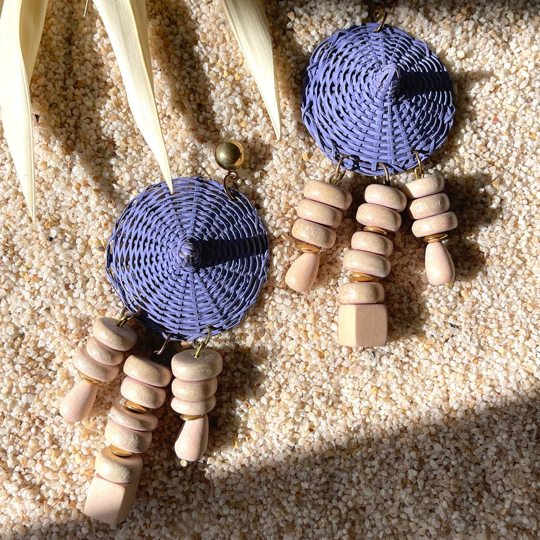 A pair of vintage costume jewelry wicker woven basket earrings with wooden bead dangles shown on sand