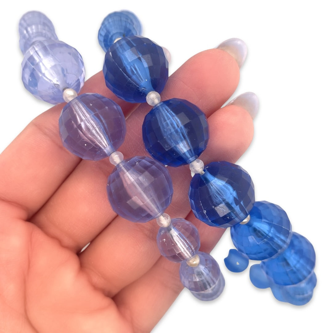 Two rows of light and dark blue plastic crystal beads from a vintage 1950s era beaded necklace shown in hand for scale