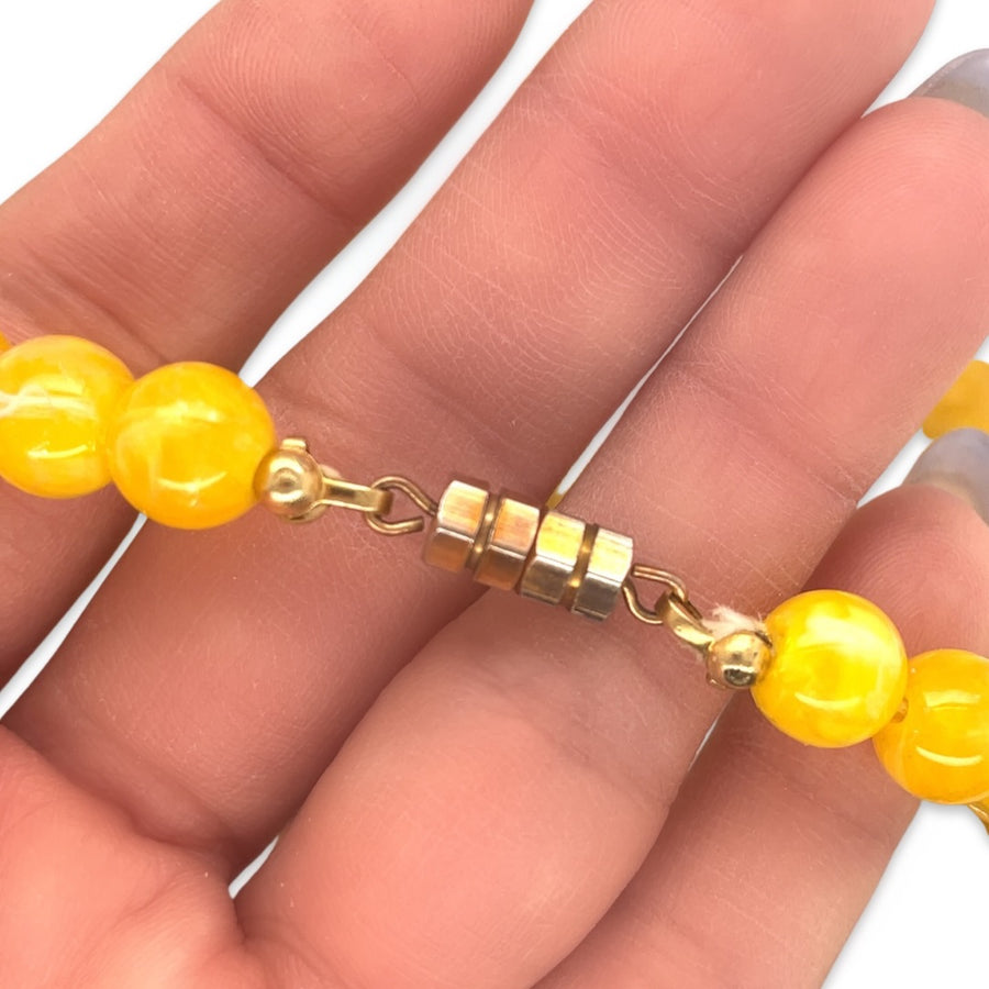 A close-up of the clasp of a vintage 1950s Mid Century era orange and yellow beaded necklace
