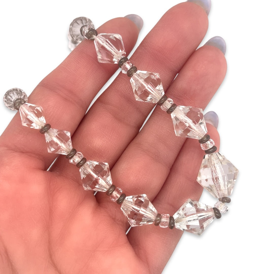 A vintage 1950s Mid Century era costume jewelry beaded necklace with plastic clear crystal beads and silver metal stations shown in hand for scale