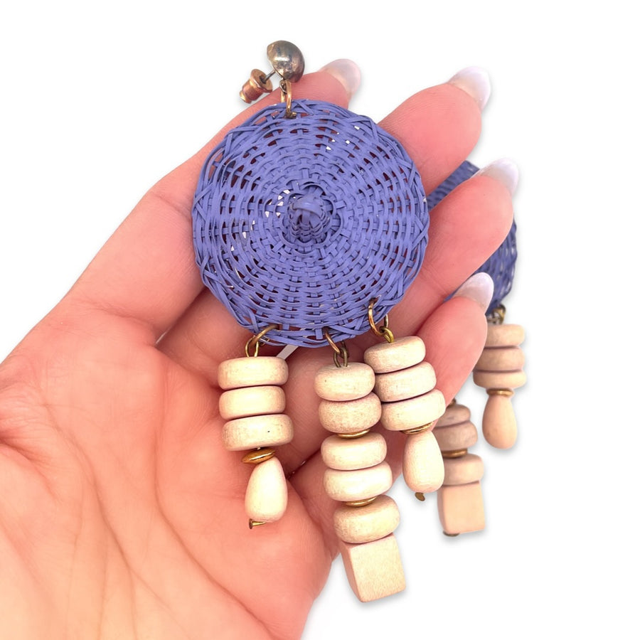 A close-up of a pair of vintage blue wicker woven basket earrings with white wood bead dangles