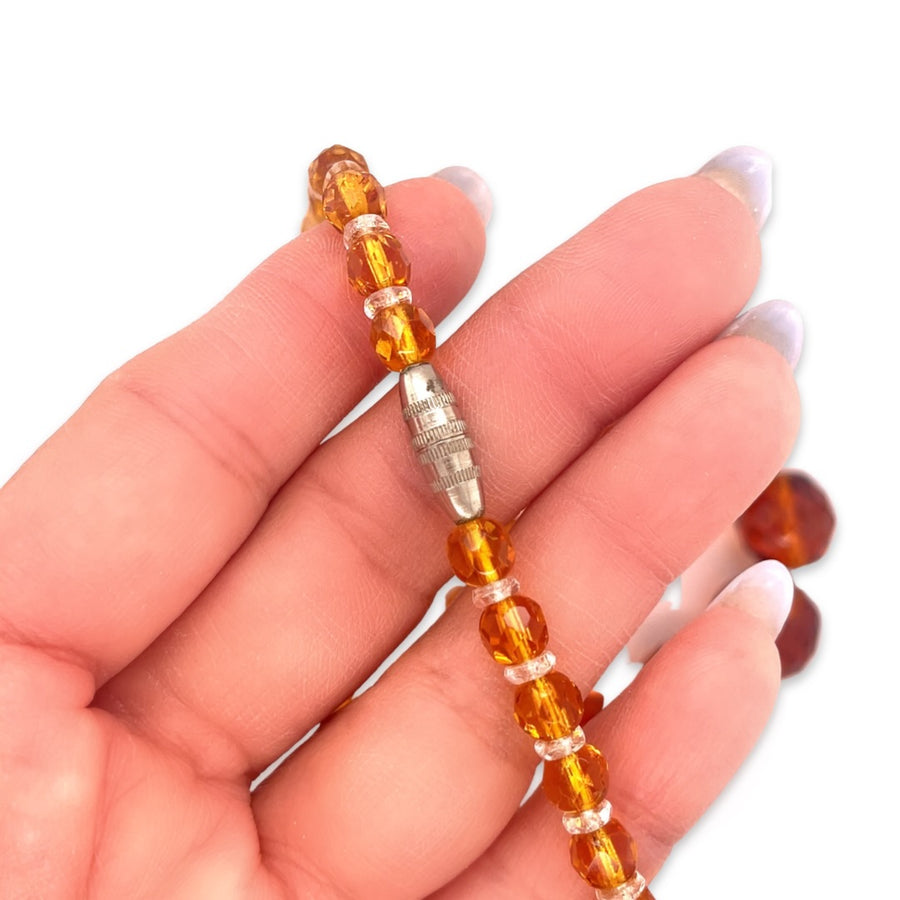 A close-up of the silver clasp on a 1920s vintage Art Deco flapper necklace with orange beads