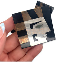 A vintage 1980s costume jewelry brooch/pendant showing an Egyptian pharaoh in profile in black and gold and silver in a square shape, in hand for scale
