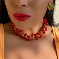 A red and gold-tone plastic nautical style choker necklace worn with gold earrings