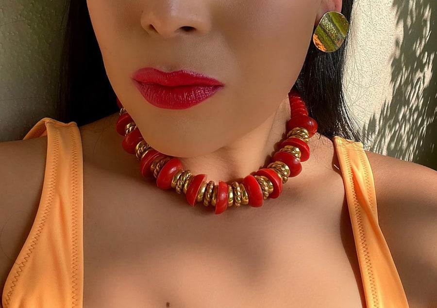 A red and gold-tone plastic nautical style choker necklace worn with gold earrings