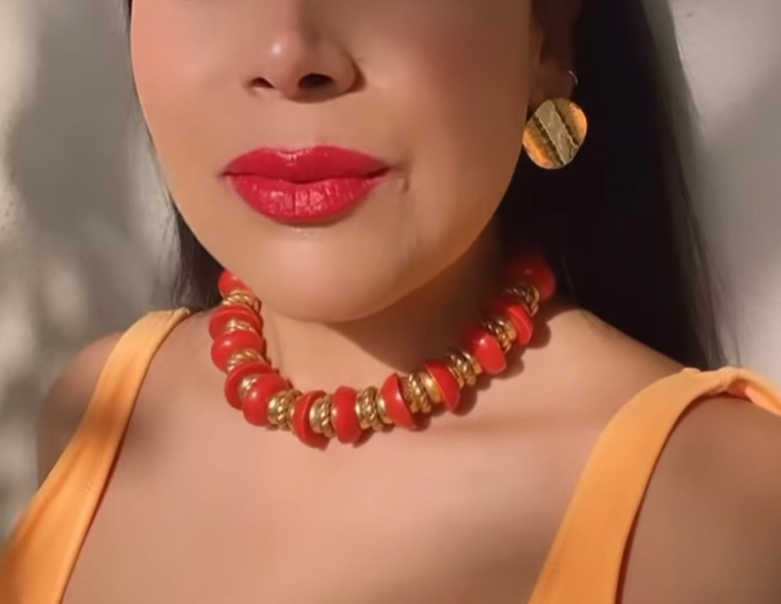 A vintage 1980s nautical style necklace in red and gold-tone plastic worn with a red lip and gold earrings