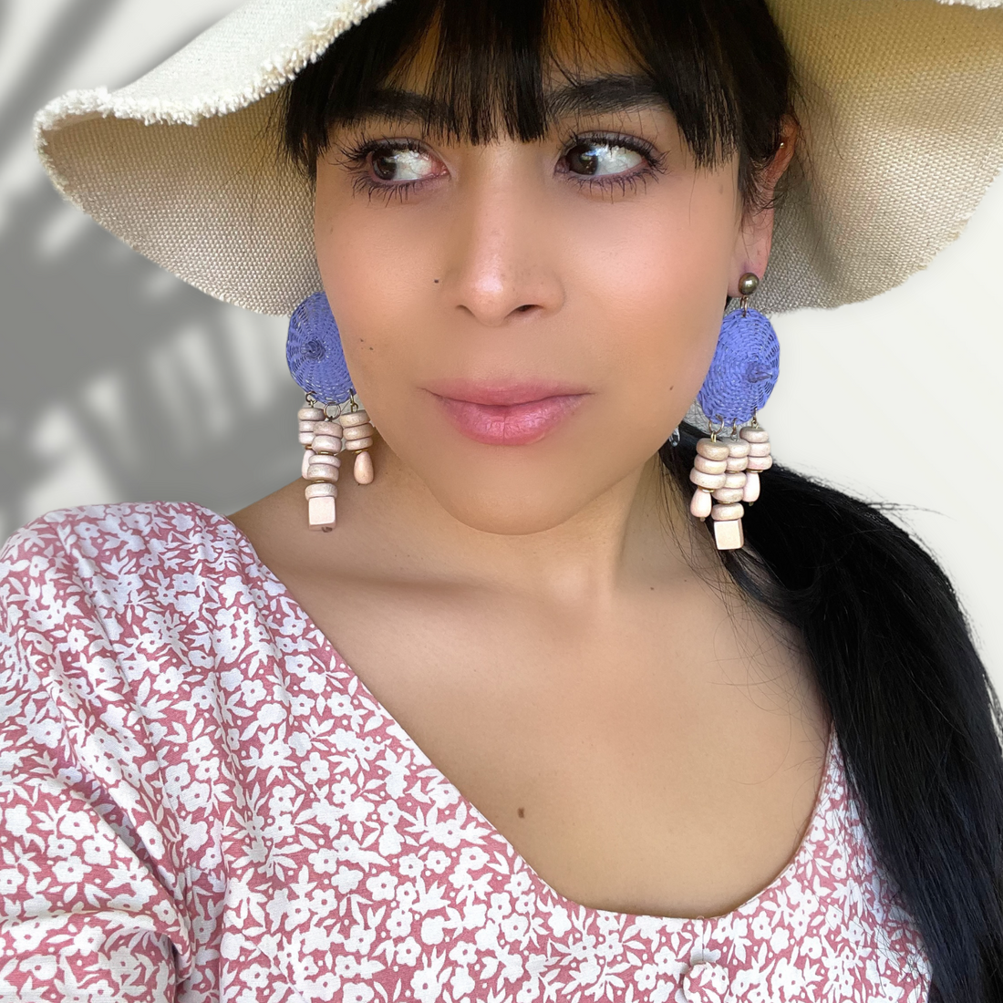 A woman with dark hair wearing a pair of vintage costume jewelry blue wicker woven earrings with white wood bead dangles