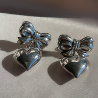 a pair of vintage sterling silver earrings with large bows and dangling puffy hearts