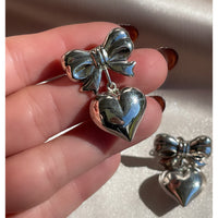 a pair of vintage sterling silver earrings with large bows and dangling puffy hearts