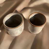 A pair of beige and brown speckled handmade pinched cups or vases