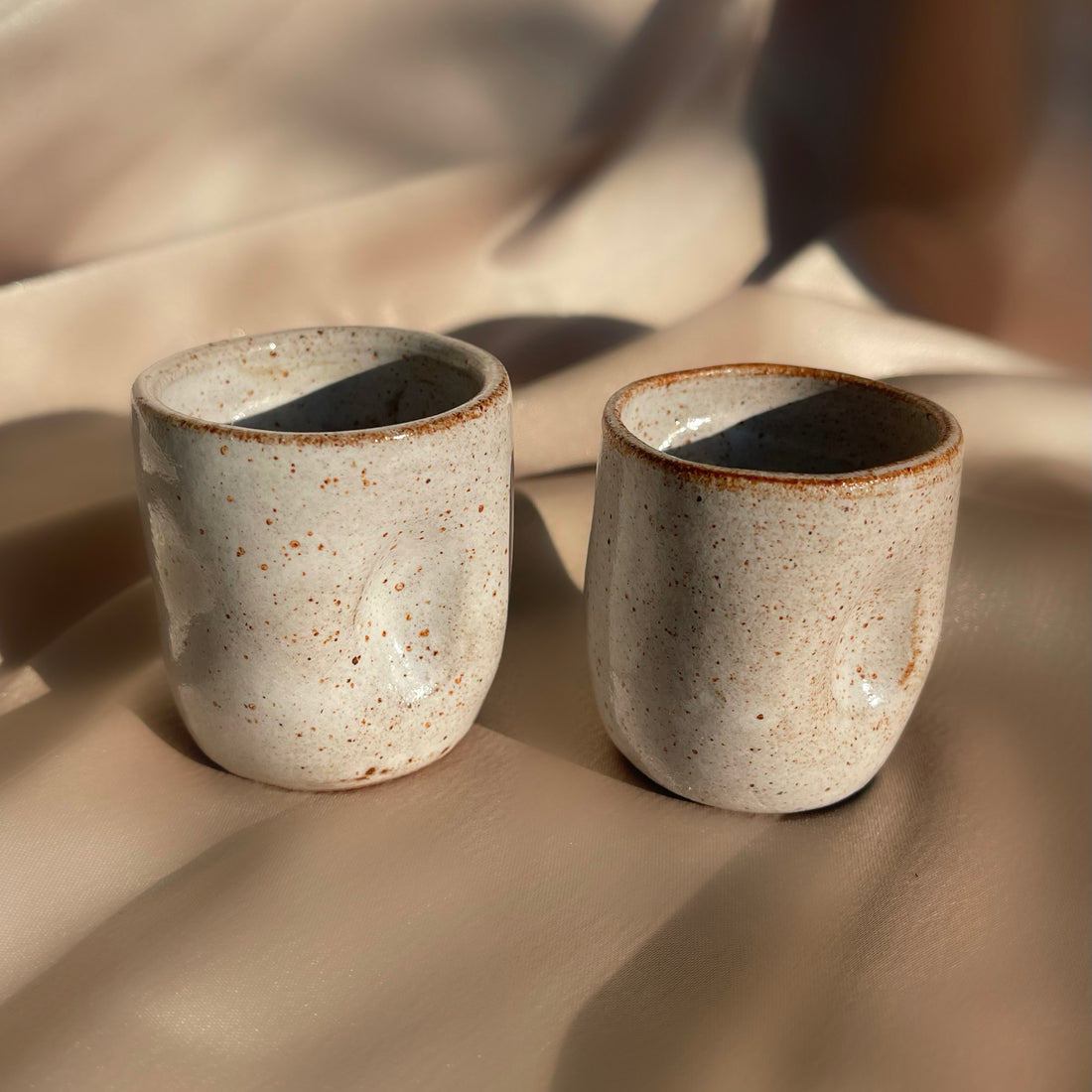 A pair of beige and brown speckled handmade pinched cups or vases