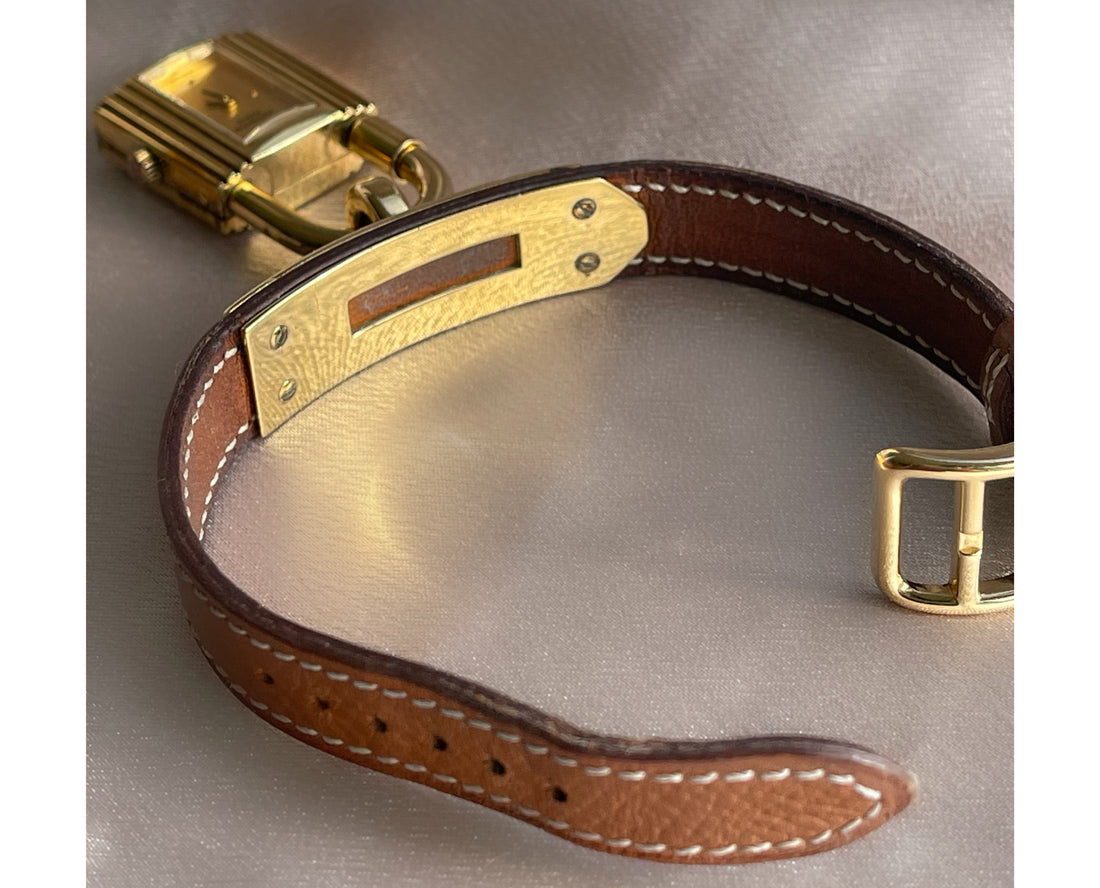 A vintage Hermès Paris circa 2000's mid aughts Kelly style lock wristwatch with a brown leather strap and gold-plated hardware