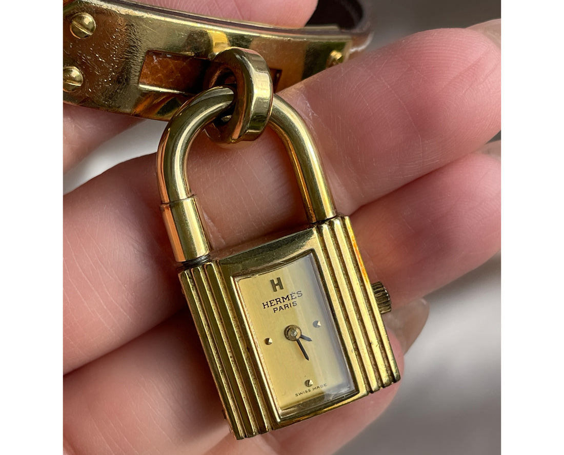 A vintage Hermès Paris circa 2000's mid aughts Kelly style lock wristwatch with a brown leather strap and gold-plated hardware